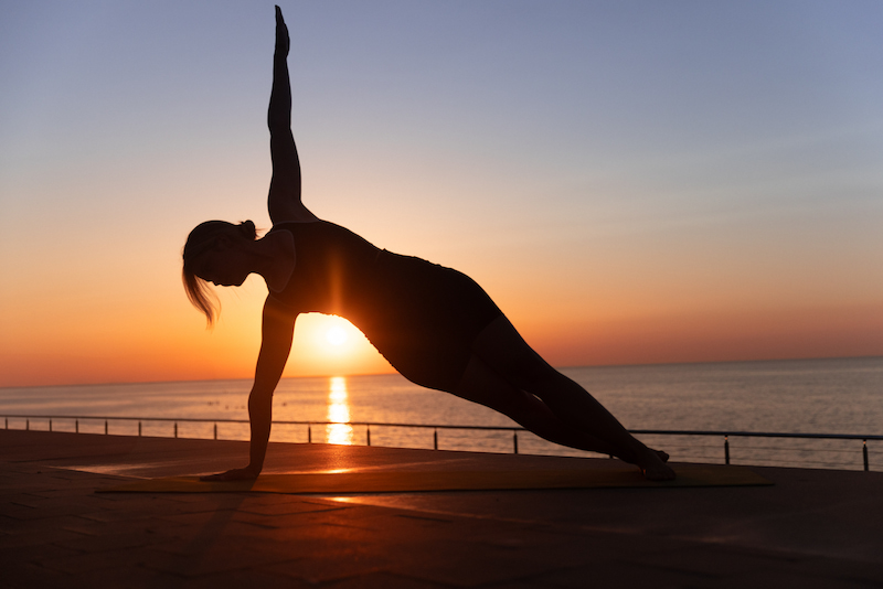 mujer haciendo postura de yoga con el amanecer de fondo