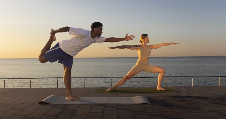 Dos personas haciendo posturas de yoga en verano con el mar detrás de ellos