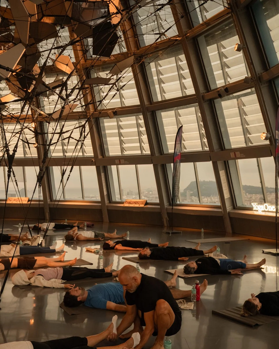 Participantes practicando yoga sobre sus esterillas en el Mirador Torre Glòries, con los ventanales y Barcelona al fondo.