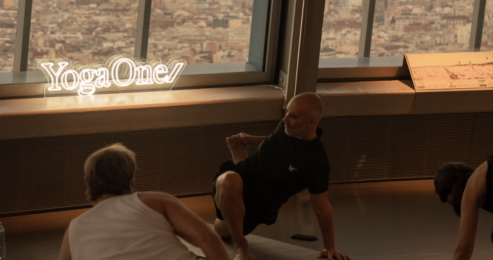Participantes practicando yoga durante Sky Yoga Barcelona en el Mirador Torre Glòries, con vistas a la ciudad y el logotipo de YogaOne.
